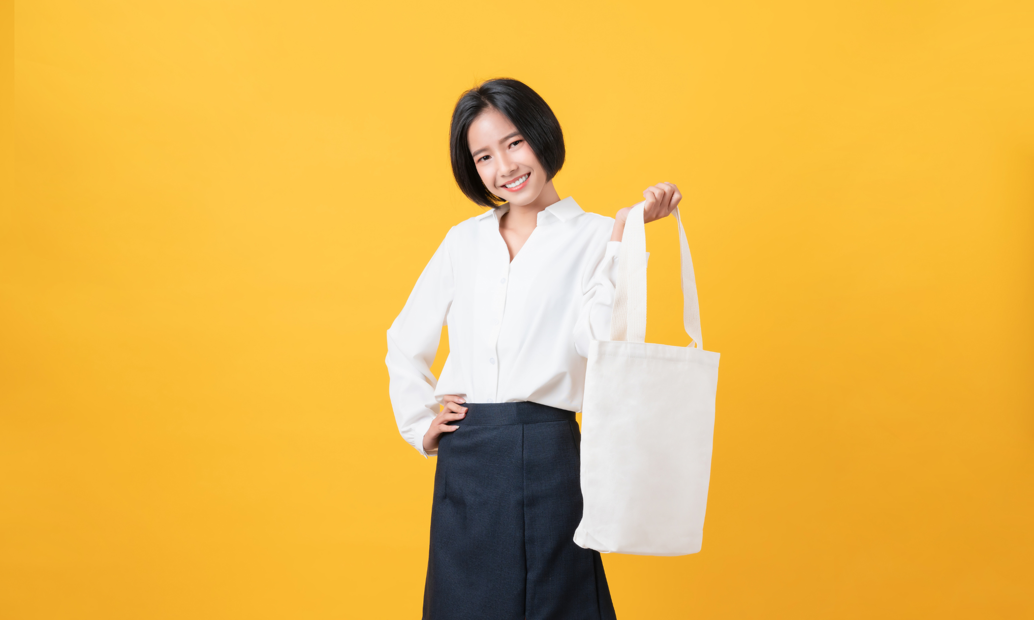 woman smiling while holding tote bag in a yellow background